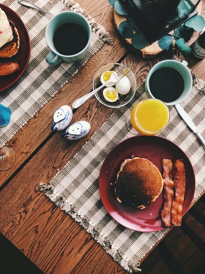 烤面包放在圆形的红色陶瓷盘上，靠近一杯橙汁、一杯咖啡和煮鸡蛋
